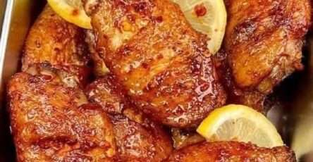 Ailes de poulet dorées nappées de sauce miel-citron, servies chaudes, parsemées de sésame et d’oignons verts sur plat blanc.