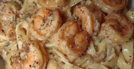 Assiette de fettuccine Alfredo nappées de sauce crémeuse et garnies de crevettes roses et persil frais, servies bien chaudes.