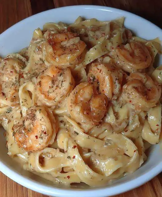 Assiette de fettuccine Alfredo nappées de sauce crémeuse et garnies de crevettes roses et persil frais, servies bien chaudes.