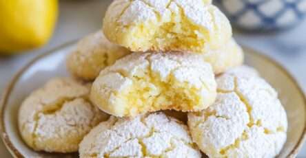 Biscuits crinkle au citron, jaunes et craquelés, posés sur une grille de refroidissement, enrobés de sucre glace, avec des zestes de citron frais.