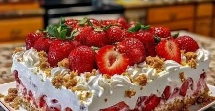 Gâteau aux fraises ultra moelleux recouvert de crème, de fraises fraîches et d’un crumble rose croquant, présenté en parts sur une assiette blanche.