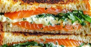 Croque doré au saumon fumé et roquette, coupé en deux, servi sur assiette avec salade verte et rondelles de citron.