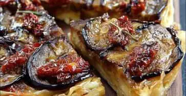 Tatin d’aubergines aux tomates séchées, dorée et fondante, servie sur une assiette blanche avec salade verte et herbes fraîches.