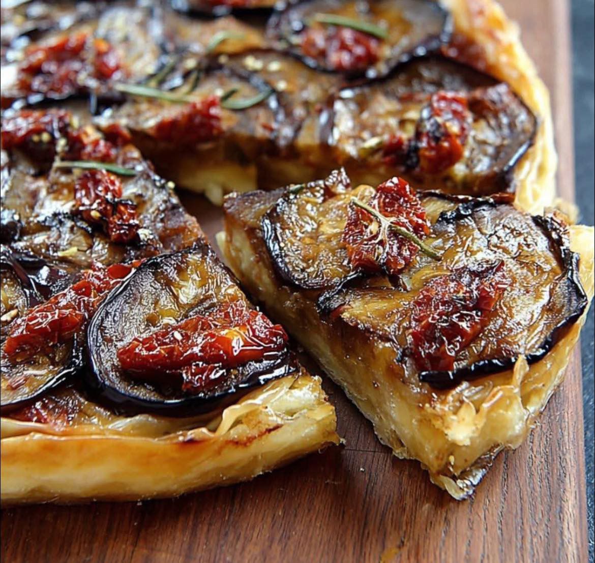 Tatin d’aubergines aux tomates séchées, dorée et fondante, servie sur une assiette blanche avec salade verte et herbes fraîches.