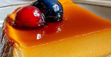 Flan pâtissier doré aux mirabelles sur pâte brisée, découpé en parts, décoré de fruits rouges, présenté sur une assiette blanche.
