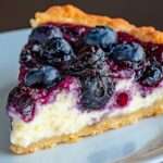 Tarte au fromage blanc garnie de myrtilles brillantes et nappée de confiture, servie sur une table en bois avec quelques fruits frais.