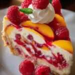 Part de cheesecake sans cuisson aux pêches et framboises avec base biscuitée et fruits frais en décoration.