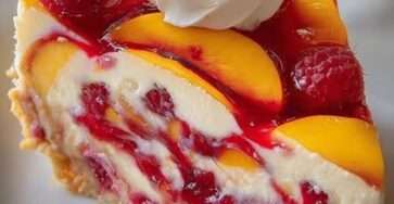Part de cheesecake sans cuisson aux pêches et framboises avec base biscuitée et fruits frais en décoration.
