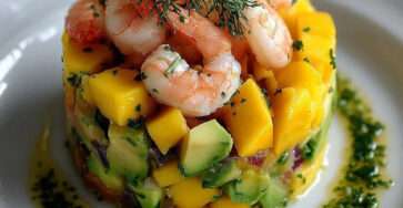 Tartare de crevettes, avocat et mangue dressé en cercle, décoré de feuilles de coriandre et de quartiers de citron vert.