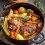 Jarret de porc braisé servi avec légumes fondants dans une cocotte en fonte.