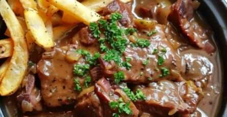 Carbonade flamande servie dans une cocotte, nappée de sauce brune, accompagnée de frites croustillantes.
