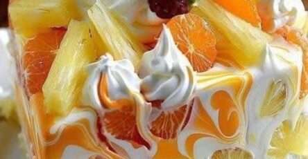 Cheesecake sans cuisson à l’orange et à l’ananas, garni de crème fouettée, tranches d’orange et morceaux d’ananas, sur base de biscuits Graham dorés.
