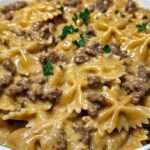 Assiette de pâtes papillon à la viande hachée et sauce crémeuse au parmesan, décorée de persil frais et servie chaude dans une poêle rustique.