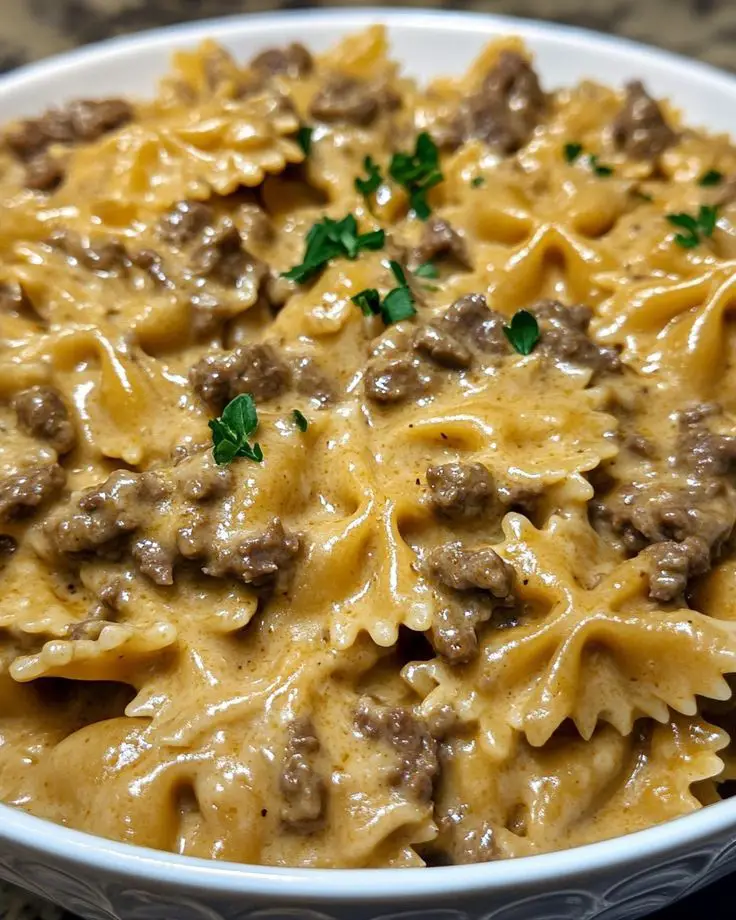 Assiette de pâtes papillon à la viande hachée et sauce crémeuse au parmesan, décorée de persil frais et servie chaude dans une poêle rustique.