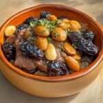 Tajine marocain d’agneau mijoté aux pruneaux, amandes grillées et miel, servi avec coriandre fraîche et semoule.