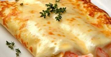 Plat de crêpes gratinées aux crevettes, moules et calamars, nappées de béchamel et gratinées au fromage doré, servies avec du persil frais dans un plat à gratin chaud.