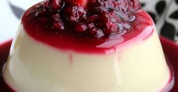 Panna cotta légère à la vanille servie dans une verrine, nappée d’un coulis de fruits rouges brillant et décorée de framboises fraîches et de menthe.