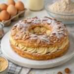 Paris-Brest classique à la praline – couronne de pâte à choux dorée garnie d’une crème pralinée onctueuse, décorée d’amandes effilées et de sucre glace, servie sur un plat blanc élégant.