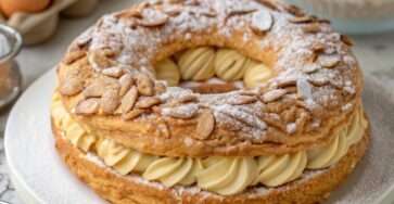 Paris-Brest classique à la praline – couronne de pâte à choux dorée garnie d’une crème pralinée onctueuse, décorée d’amandes effilées et de sucre glace, servie sur un plat blanc élégant.