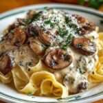 Tagliatelles aux champignons et à la crème fraîche servies dans une assiette creuse, garnies de persil et de parmesan râpé.