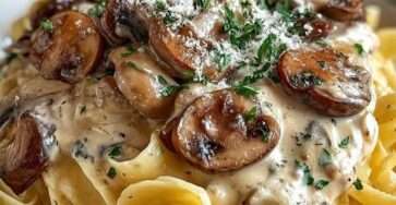 Tagliatelles aux champignons et à la crème fraîche servies dans une assiette creuse, garnies de persil et de parmesan râpé.