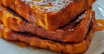 Tranches de pain perdu dorées nappées de sirop d’érable, servies avec crème fouettée et épices de citrouille sur une assiette d’automne.
