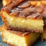 Gâteau moelleux frangipane au rhum doré, saupoudré de sucre glace et garni d’amandes effilées sur une assiette de dessert.