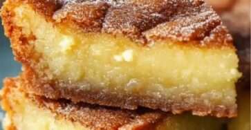 Gâteau moelleux frangipane au rhum doré, saupoudré de sucre glace et garni d’amandes effilées sur une assiette de dessert.