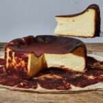 Cheesecake basque doré et caramélisé, au centre crémeux et tremblotant, présenté sur du papier sulfurisé rustique dans un moule à charnière.