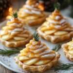 Tartelettes feuilletées garnies de brie, pommes fines en spirale et filet de caramel, décorées d’un brin de romarin.