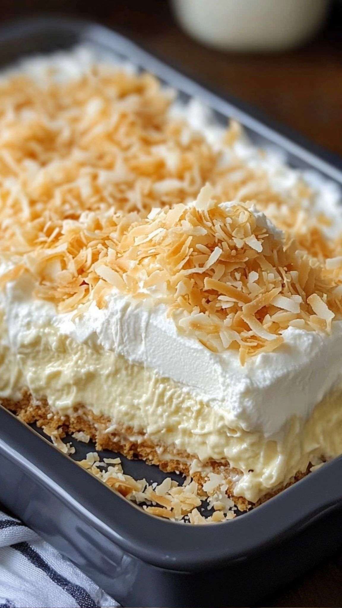 Photo d’un dessert Coconut Cream Lush en couches crémeuses avec croûte de biscuits Graham, crème fouettée et copeaux de noix de coco grillés.