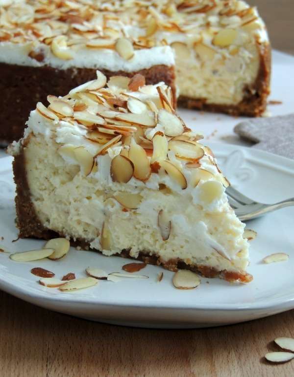 Cheesecake à l’amande et à l’Amaretto, surmonté d’amandes grillées dorées, sur fond de table en bois clair, tranché pour révéler sa texture onctueuse et dorée.