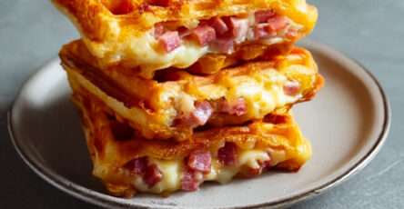 Gaufres salées dorées au jambon et fromage fondu, servies chaudes sur une assiette avec salade verte et herbes fraîches.