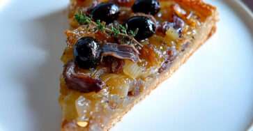 Pissaladière provençale maison aux oignons caramélisés, anchois et olives noires, dorée au four et servie sur une planche rustique en bois.