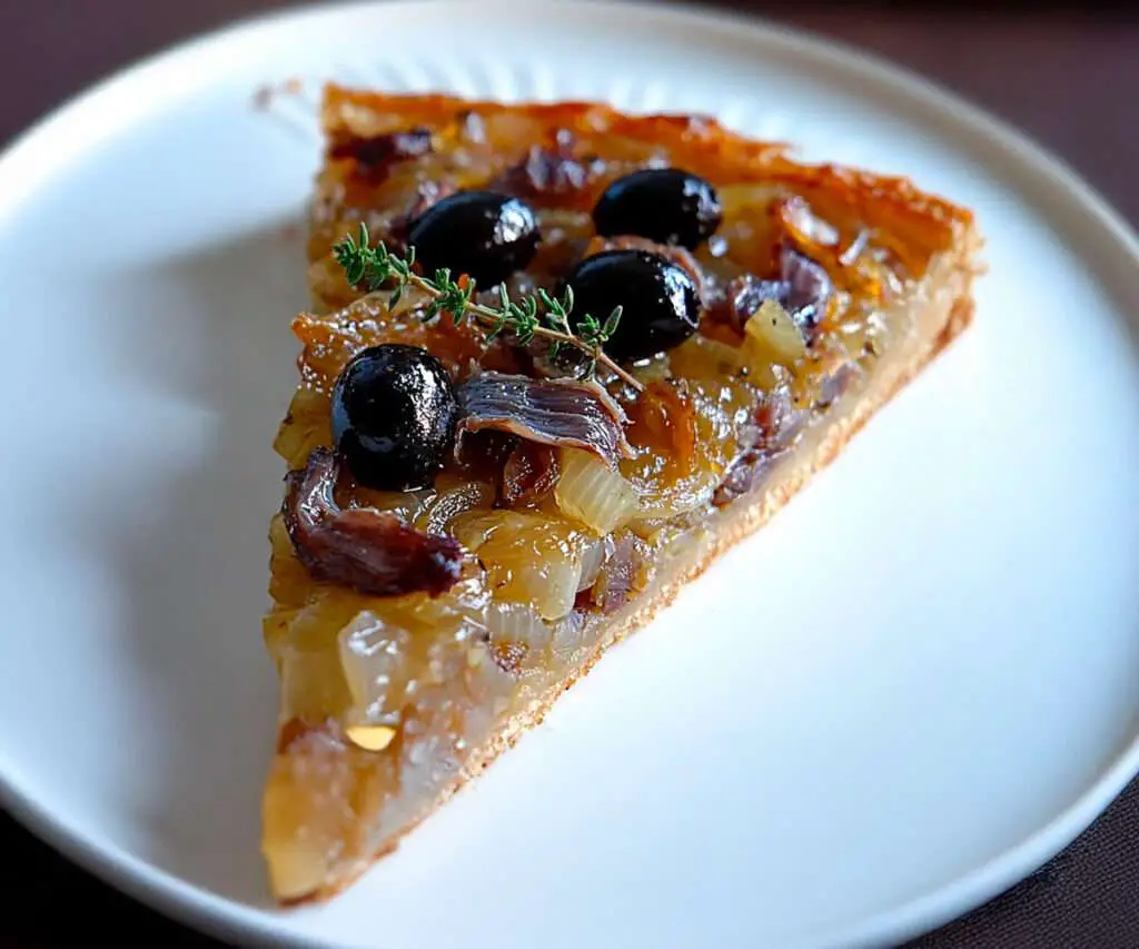 Pissaladière provençale maison aux oignons caramélisés, anchois et olives noires, dorée au four et servie sur une planche rustique en bois.