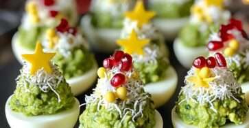 Œufs mimosa dressés en forme de petits sapins de Noël, garnis d’avocat, fromage râpé, graines de grenade et étoile de poivron jaune au sommet, sur un plat de fête.