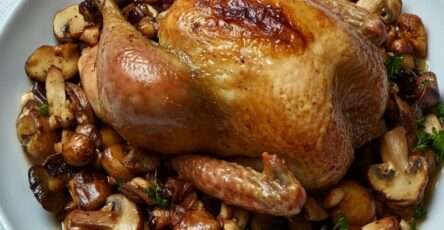 Chapon rôti doré au four, entouré de marrons caramélisés et de champignons sautés, servi dans un grand plat de fête sur une table élégamment dressée.