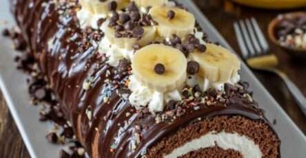 Bûche roulée chocolat banane glacée au chocolat noir brillant, décorée de rondelles de banane, pépites de chocolat et chantilly sur un plat de fête.