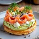 Paris-Brest salé garni de crème d’avocat citronnée et de saumon fumé, décoré de fromage frais fouetté, d’aneth et de baies roses sur une assiette de fête.