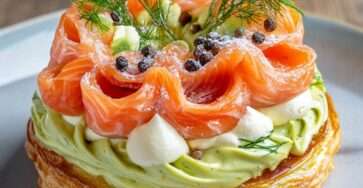 Paris-Brest salé garni de crème d’avocat citronnée et de saumon fumé, décoré de fromage frais fouetté, d’aneth et de baies roses sur une assiette de fête.