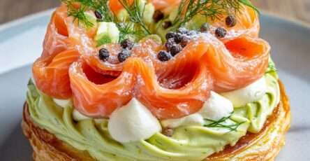 Paris-Brest salé garni de crème d’avocat citronnée et de saumon fumé, décoré de fromage frais fouetté, d’aneth et de baies roses sur une assiette de fête.