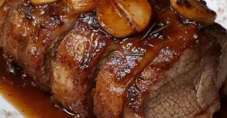 Rôti de porc caramélisé au miel tranché, nappé de sauce brillante miel-soja avec échalotes et romarin, servi dans une cocotte avec garniture.