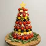 Sapin apéritif composé de tomates cerises, cubes de fromage, olives, saucisson et étoiles décoratives, monté sur un cône et décoré de romarin.
