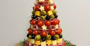 Sapin apéritif composé de tomates cerises, cubes de fromage, olives, saucisson et étoiles décoratives, monté sur un cône et décoré de romarin.