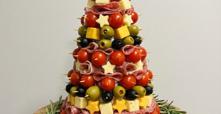 Sapin apéritif composé de tomates cerises, cubes de fromage, olives, saucisson et étoiles décoratives, monté sur un cône et décoré de romarin.