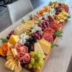 Plateau garni de fromages variés, charcuteries roulées, fruits frais, noix, crackers et herbes, présenté de manière harmonieuse pour un apéritif festif.