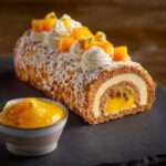 Bûche de Noël mangue passion coco glacée, décorée de dés de mangue fraîche et copeaux de coco, présentée sur un plat de fête tropical.