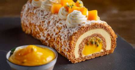 Bûche de Noël mangue passion coco glacée, décorée de dés de mangue fraîche et copeaux de coco, présentée sur un plat de fête tropical.