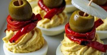 Plateau d’œufs farcis méditerranéens décorés avec olives, poivrons rôtis et rondelles de radis, présentés en bouchées apéritives colorées.