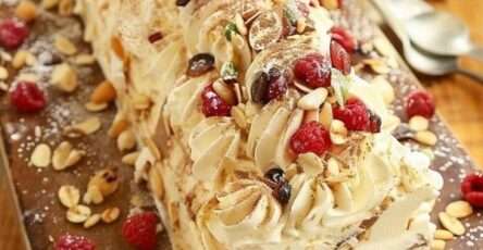 Bûche roulée garnie de crème au mascarpone et framboises, décorée d’amandes effilées, fruits secs et sucre glace sur un plat de fête.